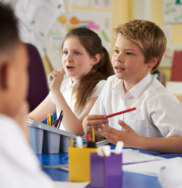 Two children listening attentively in class. They are working on pieces paper at a school desk