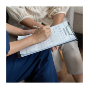 A close up of a woman taking note on a clipboard. There is another person sitting next to her.