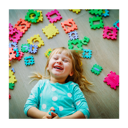 A smiling child on the floor looking at the camera above. There are coloured letters and number squares around her head.