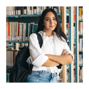 A female students leaning against a bookcase. She has her arms crossed and is smiling at the camera.