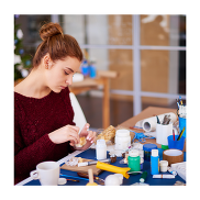 Young person crafting at a table. There are various objects on the table such as scissors, papers, pens and more.