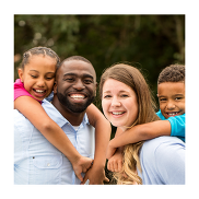 A family of two adults and two children. They are outdoors and the parents have their children on their backs.