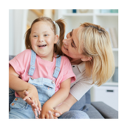 A young girl with Down's Syndrome on her mum's lap. She is smiling at the camera.