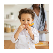 A boy of British Black ethnicity eating a piece of melon. He's holding the fruit with both hands.