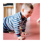 A toddler crawling in a room with a pink floor. He's wearing a white and blue stripy top.