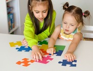Two girls playing with a puzzle on a white table.