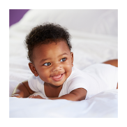 A baby on a white babygrow on a white bed. He is about 3 months old and of Black British ethnicity.