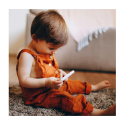 Toddler in an orange dungaree sitting on the floor looking at an object in his hands.