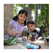 Two children painting on a table outdoors. There are different supplies on the table.