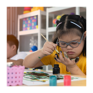 Young girl with Down's Syndrome wearing glasses painting with a brush, with paint on her hand. 