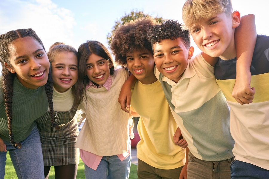 Three girls and three boys with linked arms smiling in the sunshine