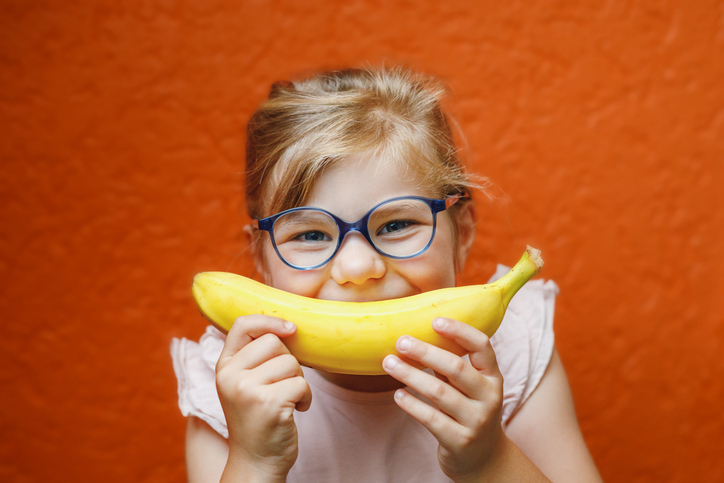 Toddler in glasses using a banana as a smile