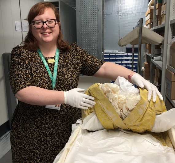 Sarah pictured with a yellow silk 18th century dress in the costume and textile store