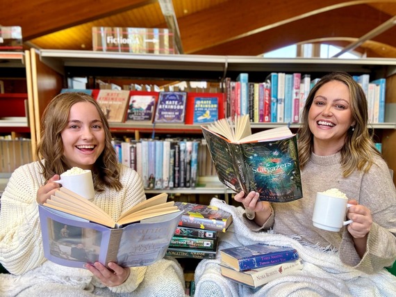 Library staff holding cups of hot chocolate and books