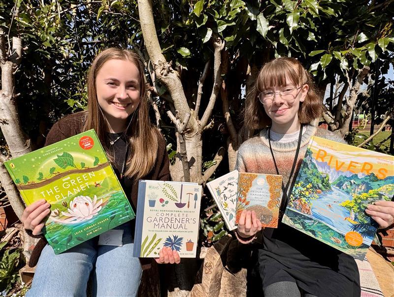 Two young people in a garden holding up library books