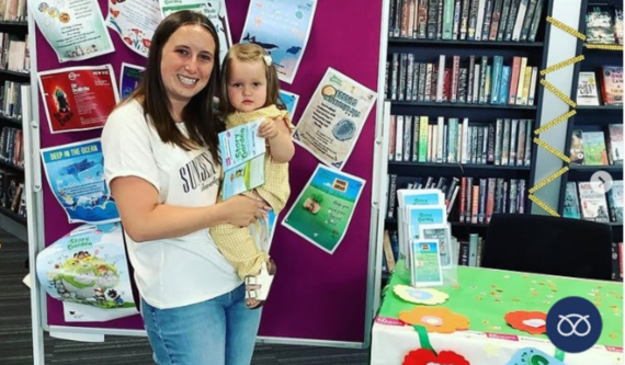mom with her child at library in front of summer reading challenge banner 
