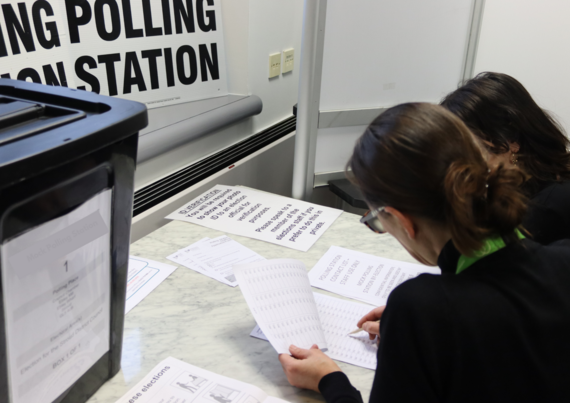 Two people examine election documents at a mock polling station