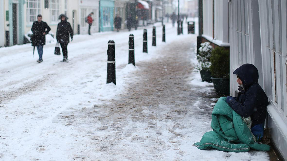 A homeless person rough sleeping at the side of a street in cold weather.