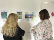 Two people looking at images on a wall and adding post-it note comments to them