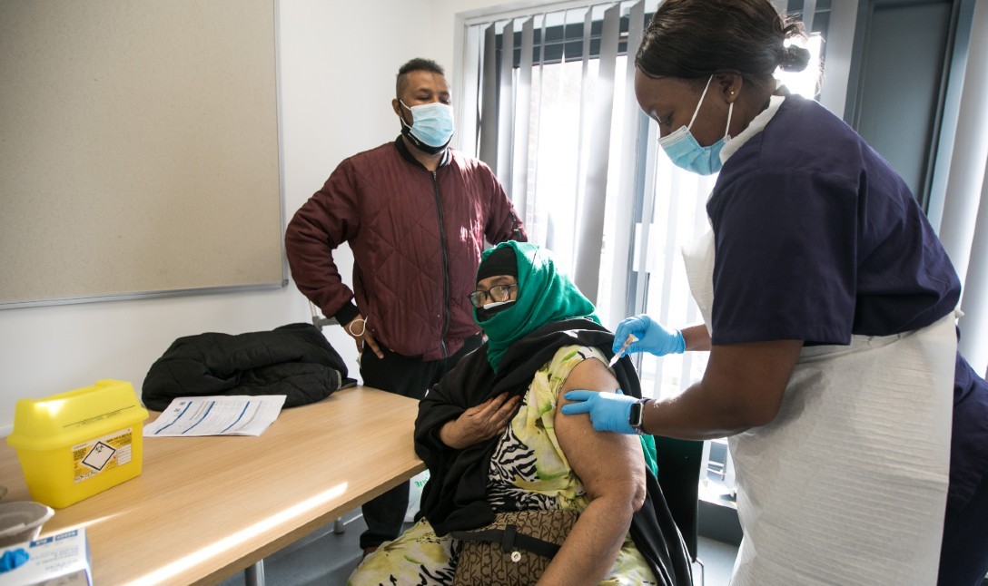 Photograph of a woman receiving a Covid-19 vaccine at Granby Hall in Tower Hamlets