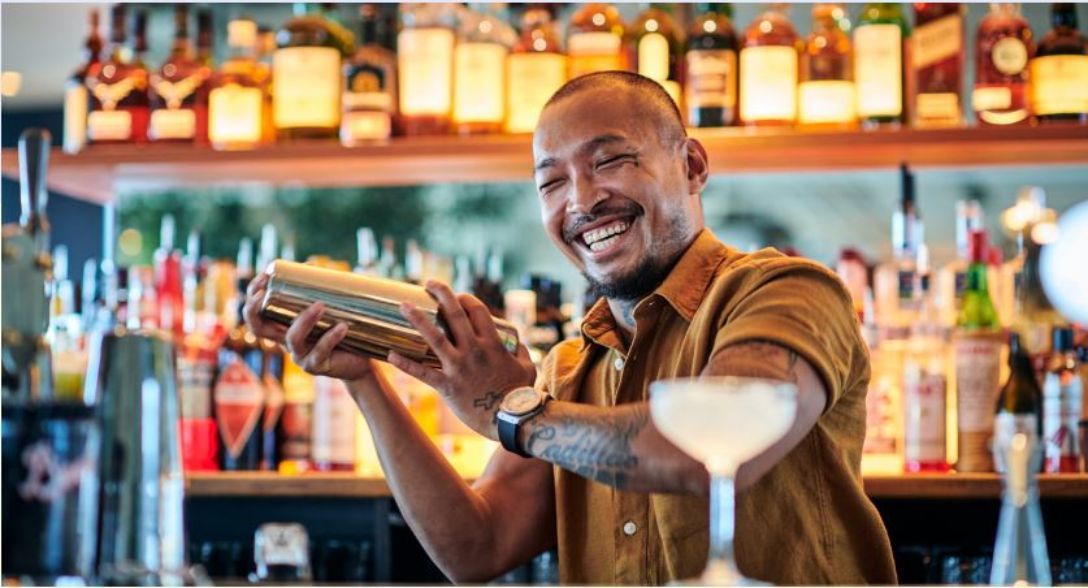 male bartender smiling whilst mixing a cocktail