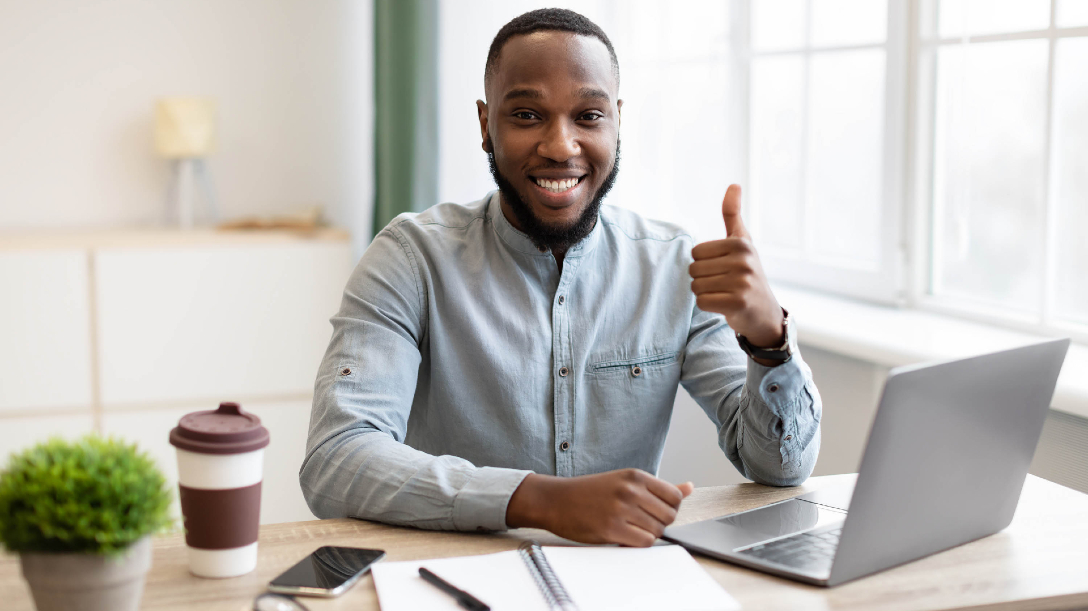 Person sitting by their desk and giving a thumbs up to the camera