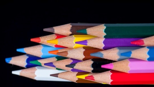 A selection of rainbow-coloured pencils arranged on a black background