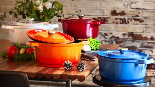 Red, yellow and blue cooking pots on a wooden kitchen top with some loose vegetables