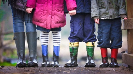 Four pairs of legs in muddy welly boots, belonging to children of different ages 
