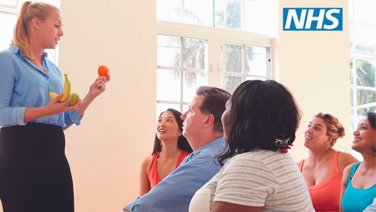 A woman holds up 2 pieces of fruit in front of a small group of men and women