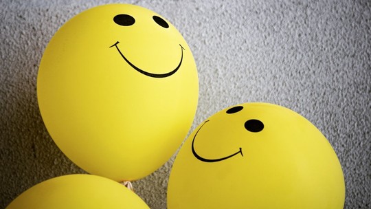 Three yellow balloons with smiley faces drawn on them in black ink