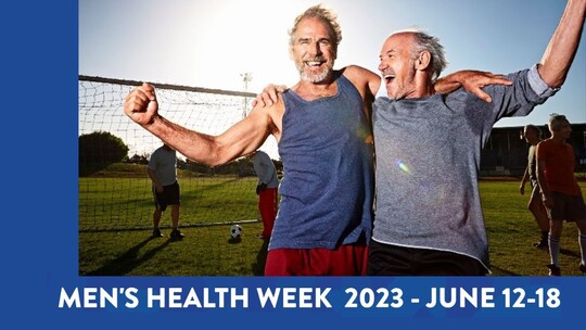 2 older men in sports clothes embracing in celebration. There is a football and football net in the background. 