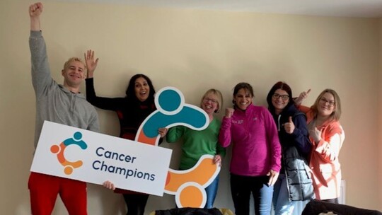 6 Cancer Champion volunteers informally posed and holding 2 cardboard cut-outs of the project logo, which is a big 'C'