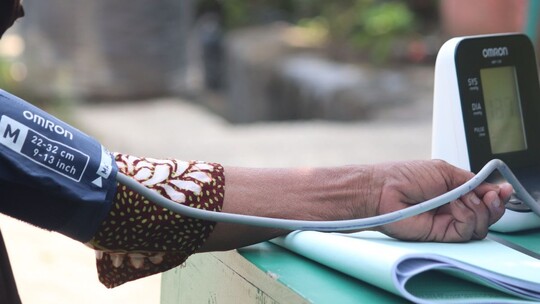 A close up photo of a person's arm resting on a table with a blood pressure monitor cuff wrapped around it and the monitor on the table