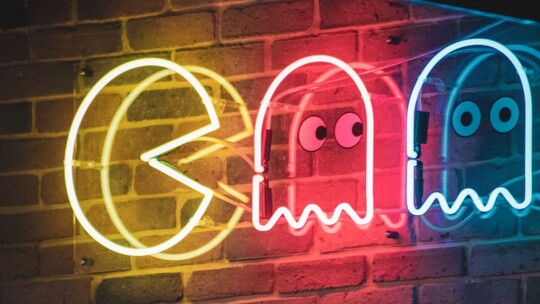 Neon lights in the shape of Pacman and two ghosts. Pacman is yellow, the ghosts are pink and blue.