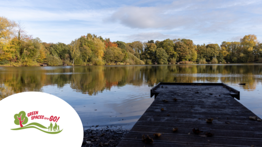 A wooden fishing platform at the edge of a pool surrounded by trees. The Green Spaces Are Go logo appears in the bottom left corner.