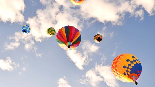 5 hot air balloons in a blue sky with white fluffy clouds, seen from below