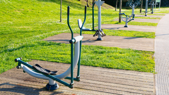 A grassy park with outdoor gym equipment on a decked area