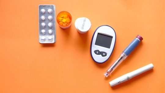 Pills, a glucose monitor and a needle laid out on an orange surface