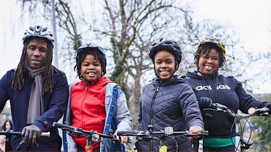 A family of four, all mounted on bicycles and smiling into the camera
