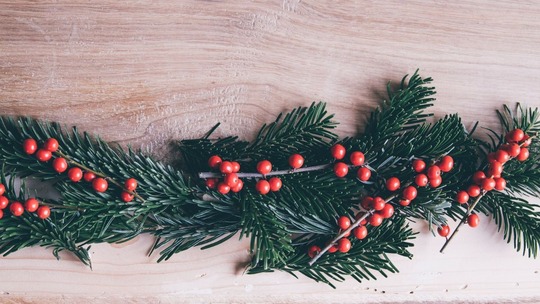 Evergreen branches and red berries laid across a wooden table top