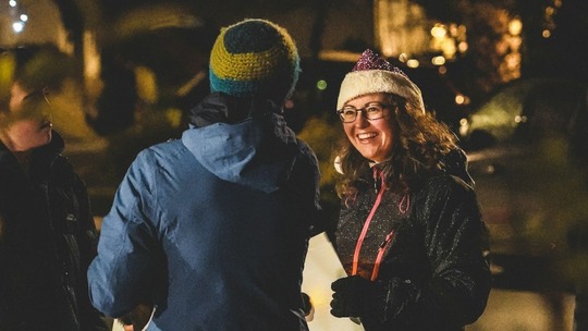 A woman and 2 men of varying ages in a residential street in the dark chatting together