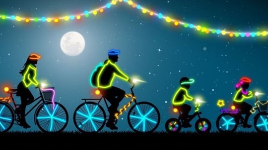 Black silhouette of 2 adults and 2 children, all on bicycles. Their bikes and helmets are decorated with neon yellow pink and green