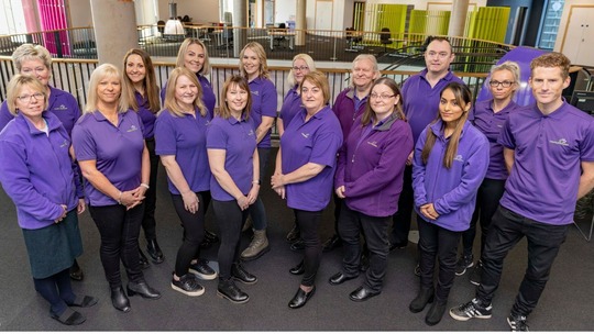 A group photo of the 16 members of the Healthy Lifestyles Team in their purple uniform t-shirts