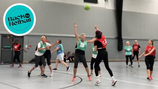 10 women of various ages playing netball in a sports hall. The Back to Netball logo appears in the top left corner.