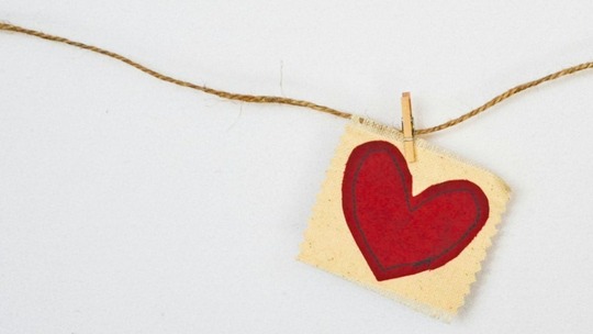 A scrap of fabric with a heart stitched onto it, pinned to a piece of string hanging against a white wall