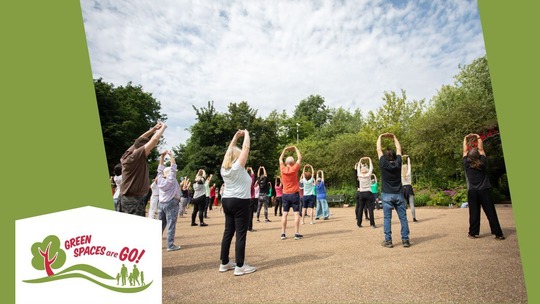A group of people doing Tai Chi together in Telford Town Park, June 2023. Green Spaces Are Go logo in bottom left corner.