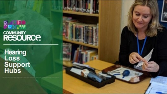 A Hearing Loss Support Hub volunteer sitting at a table in a library with hearing aid equipment in front of her 