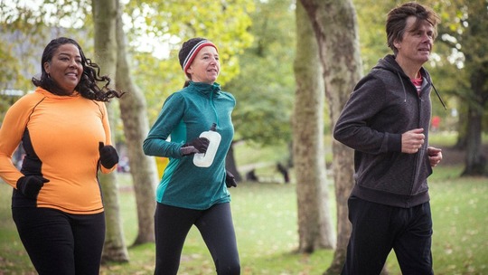 2 women and 1 man in bright clothing jogging together in a park, in the daytime.