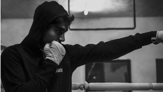 Black and white photo of a young man in a black hoodie, standing in a defensive boxing posture